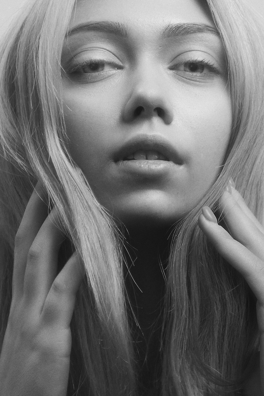 Portrait en noir et blanc d'une femme, les mains encadrant doucement son visage.